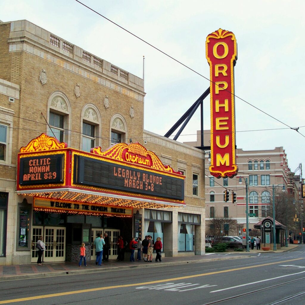 Exterior view of the Orpheum Theater in Memphis with bright neon signs advertising movies and people walking by on the street.
