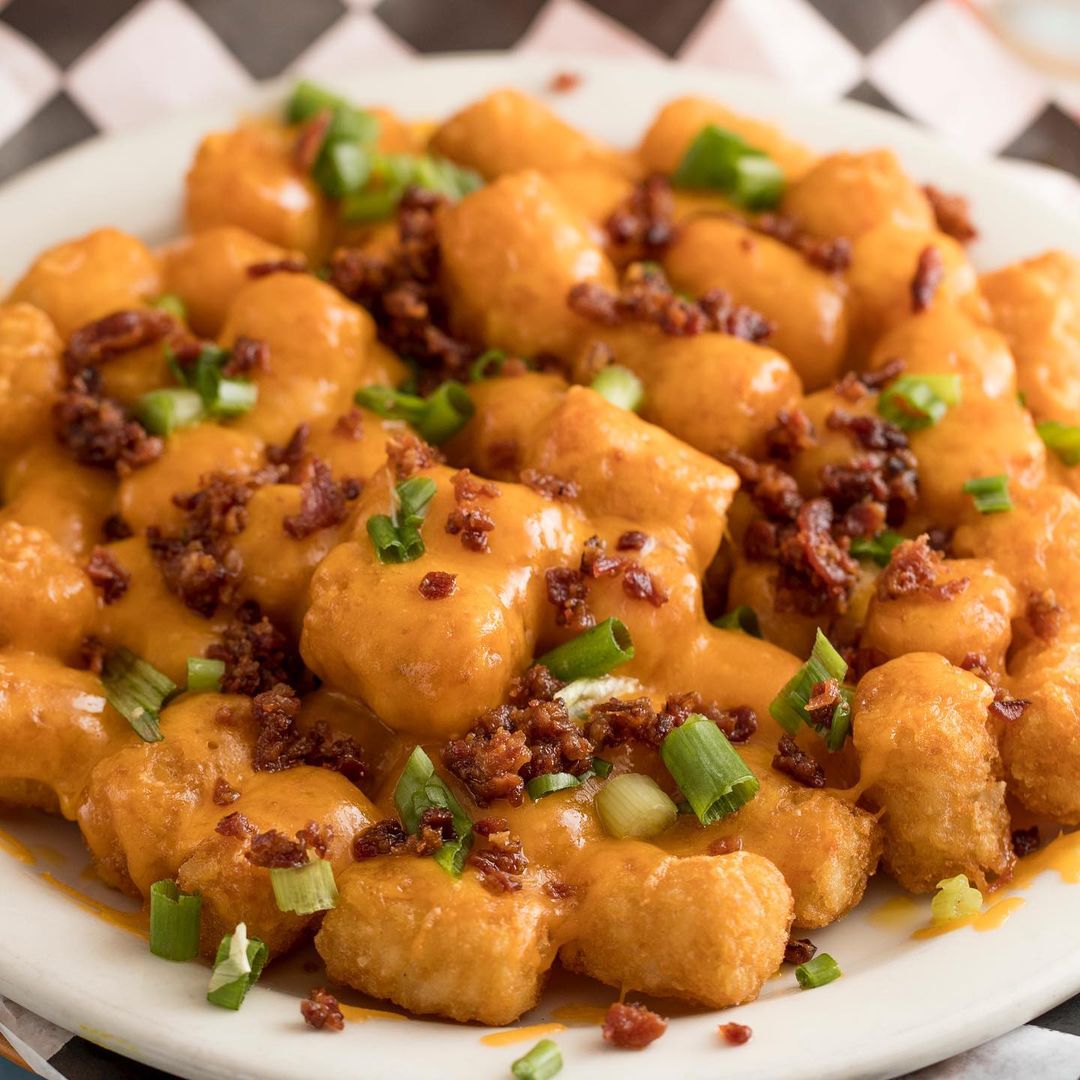 Late night bites: Tater tots adorned with bacon and green onions on a plate.
