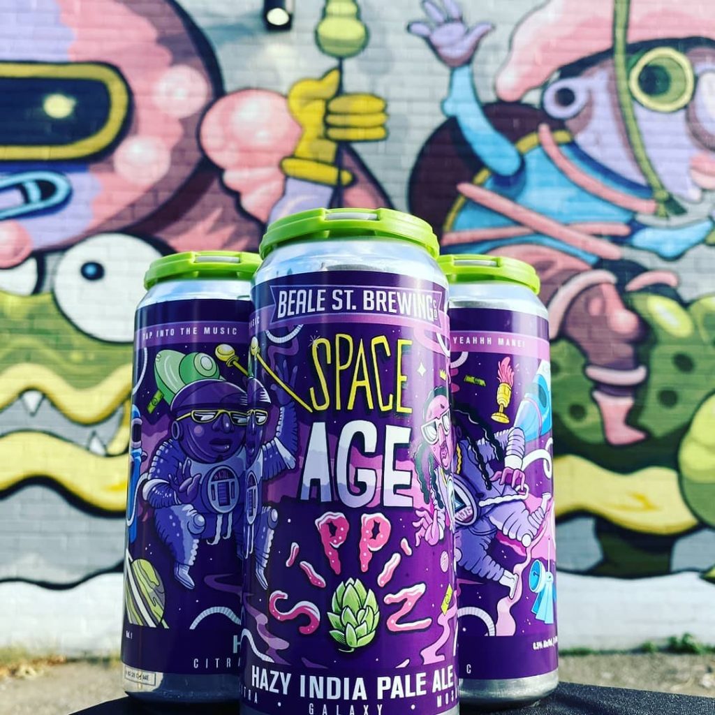 Three cans of space age ipa in front of a graffiti wall at breweries.