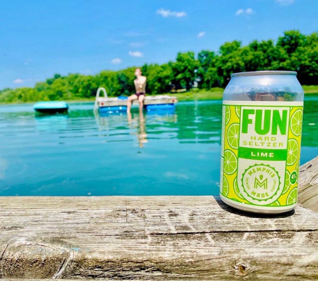 A can of fun beer sitting next to a lake.