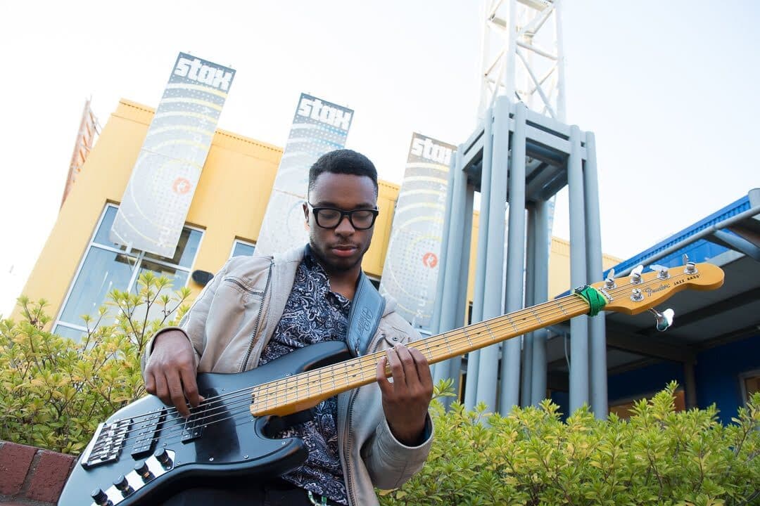 A young man playing a bass in front of a building.