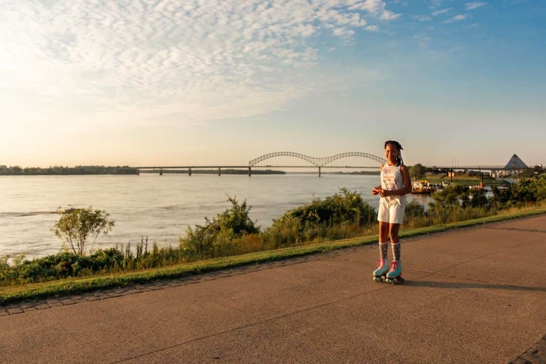A girl on a skateboard on a path near a river.