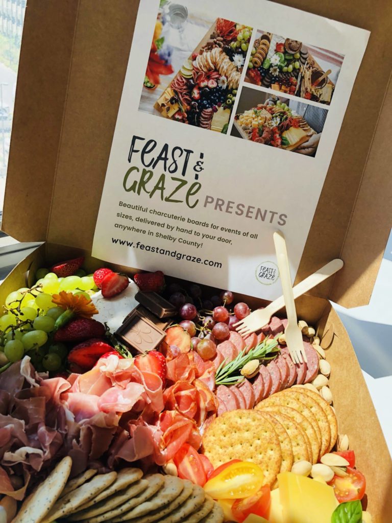 A box with a variety of meats, cheeses, and crackers.
