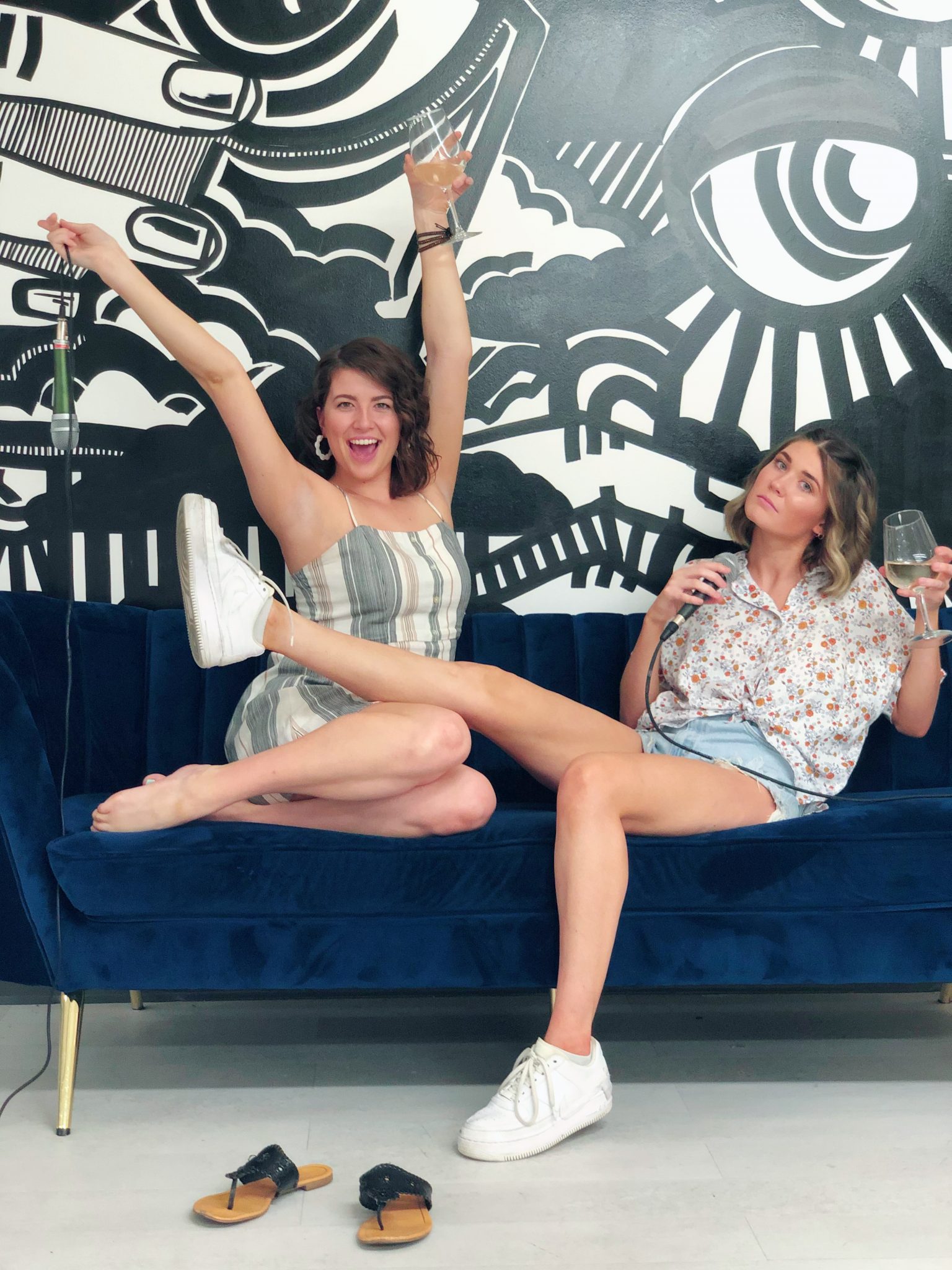 Two women sitting on a blue couch with a bottle of wine.