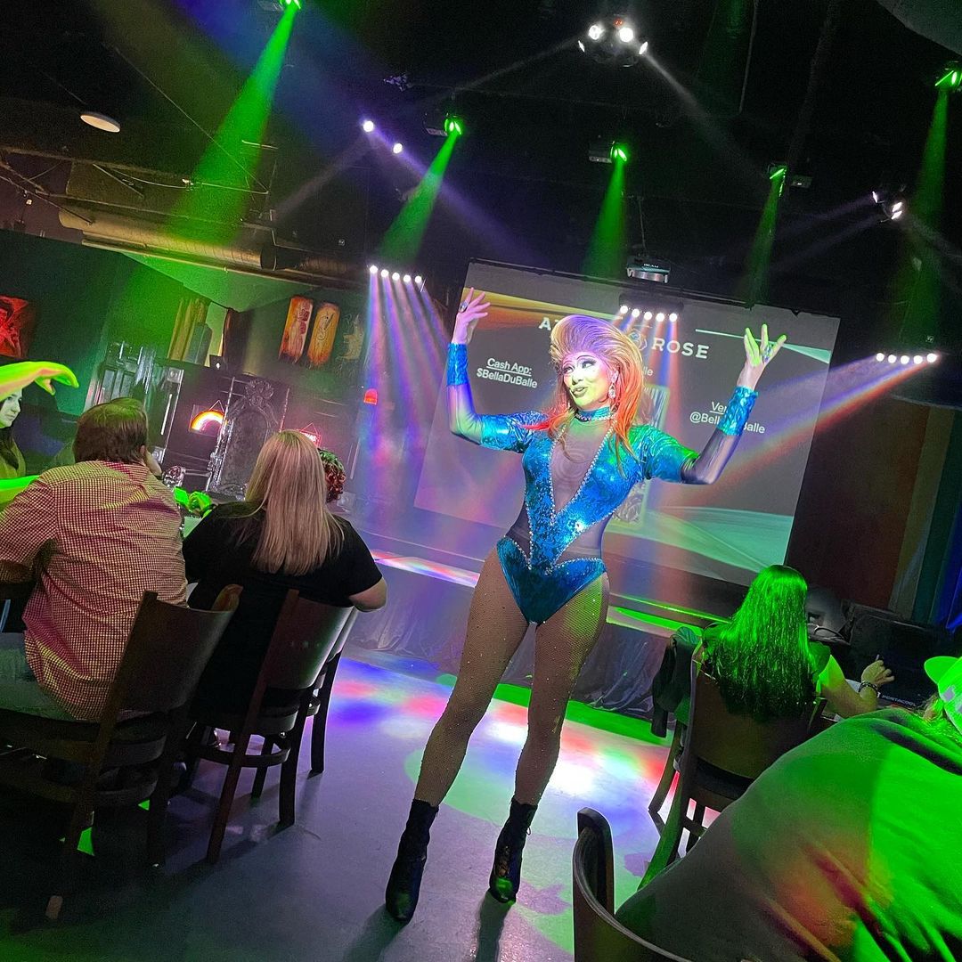 A LGBTQ+ woman is dancing in a restaurant dressed in a colorful outfit.