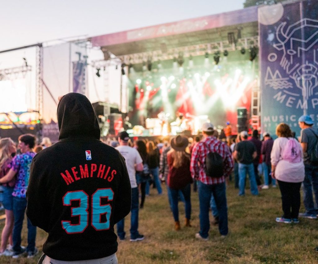 A man in a hoodie standing in front of a crowd at a fall music festival.