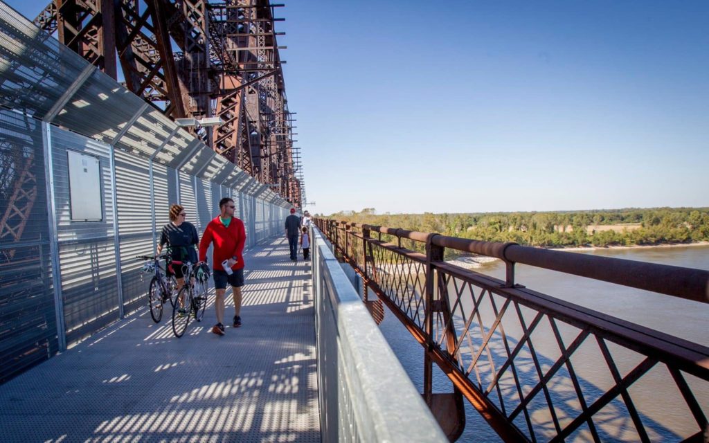 Two people biking on a bridge over a river, enjoying the Great Outdoors on Memphis Trails.