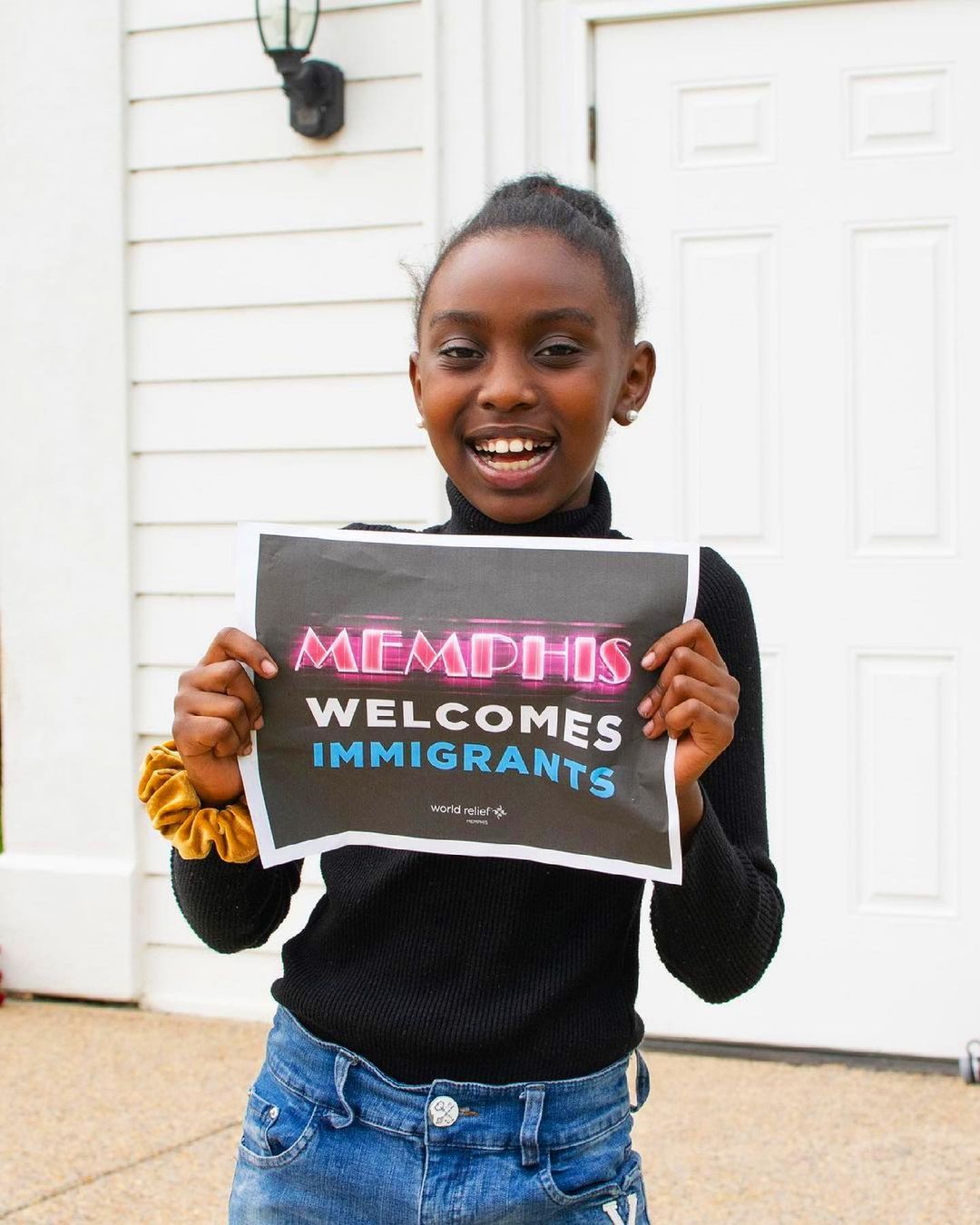 A young girl holding up a sign that says Memphis welcomes immigrants, promoting the efforts of Memphis nonprofits.