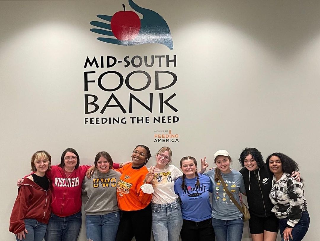 A group of girls posing in front of a sign at the Mid-South Food Bank, Memphis.