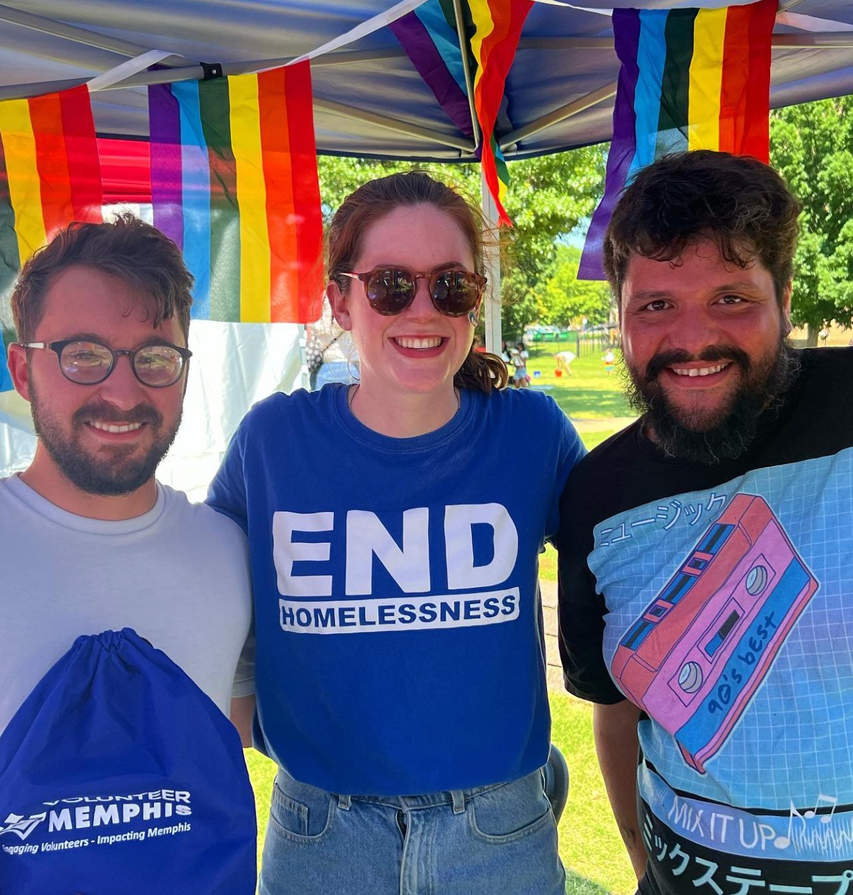 Three people standing in front of a tent with a rainbow flag representing Memphis Nonprofits.