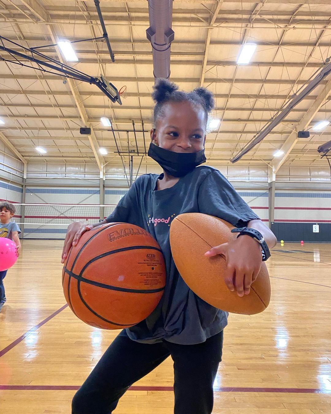 A young girl wearing a mask holding basketballs in a gym that supports Memphis nonprofits.