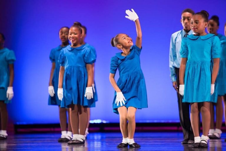 A group of children from Collage Dance Collective in blue dresses on stage.