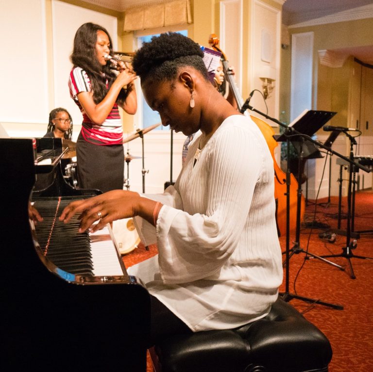 A young woman playing a piano in front of a group of musicians explores 5 ways to switch up your career in Memphis.