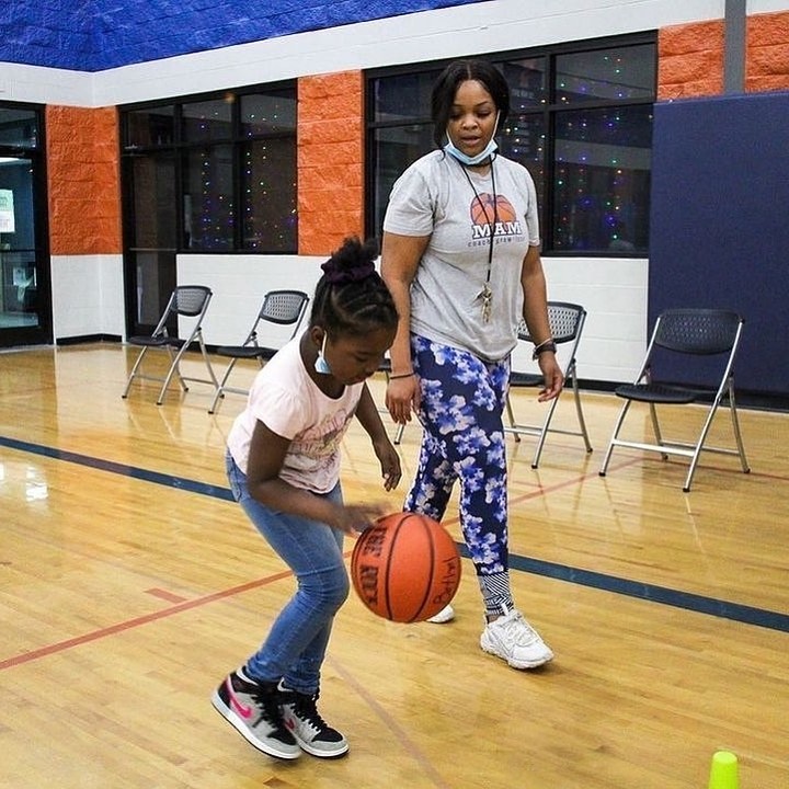 A young girl is playing basketball with a woman in a gym.