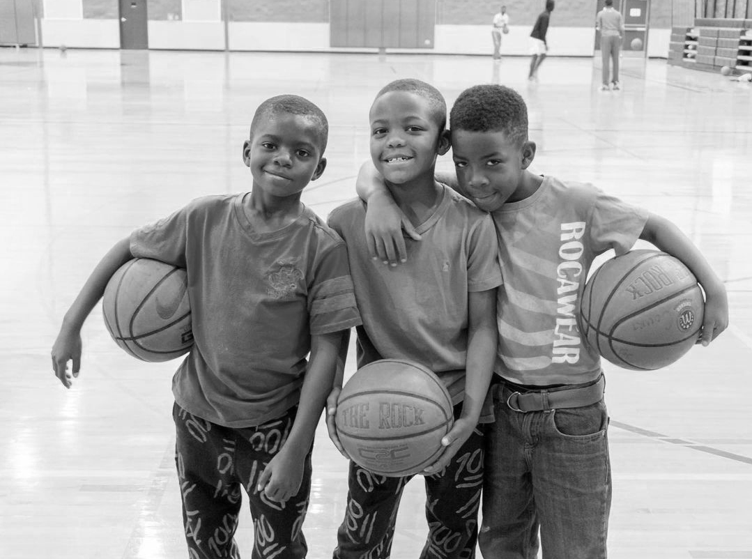 Three boys participating in the Give901 Summer Camp with basketballs in a gym.
