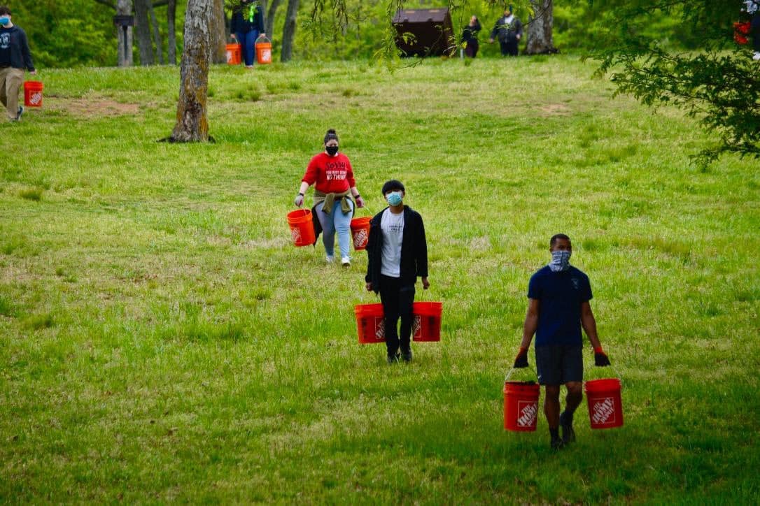 A group of volunteers carrying buckets in a field.
