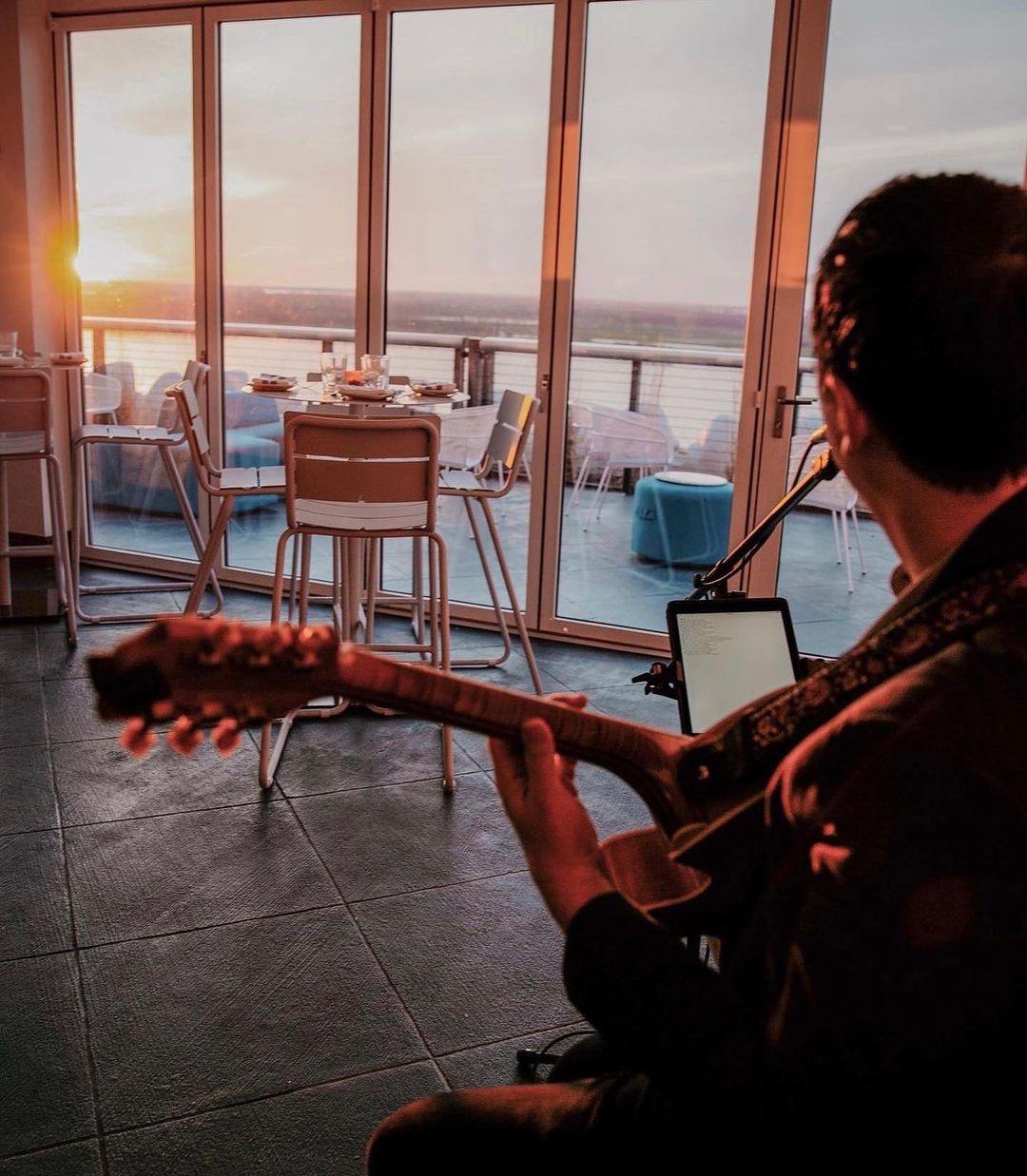 A man playing an acoustic guitar on a rooftop at sunset.