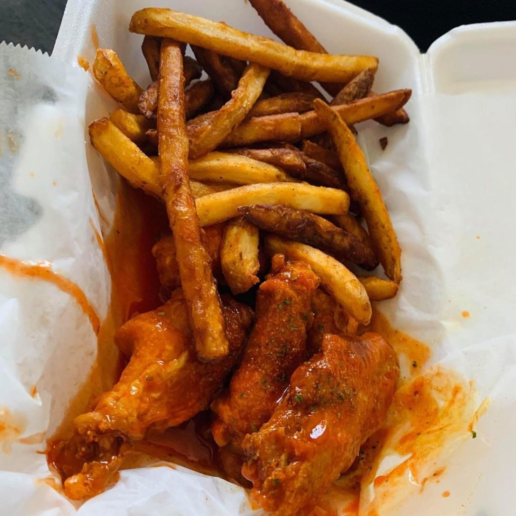Chicken wings and french fries in a plastic container.