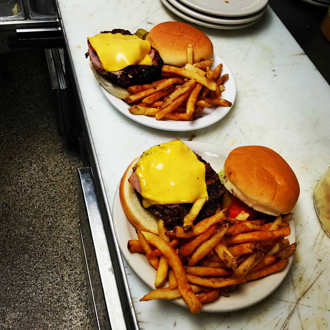 Two plates of hamburgers and french fries on a counter.