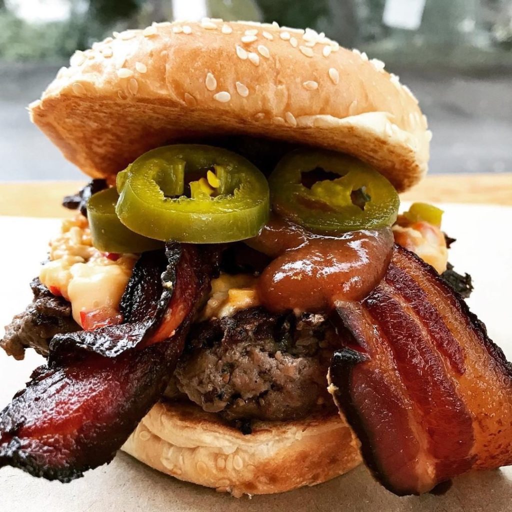 A burger with bacon and jalapenos on top.