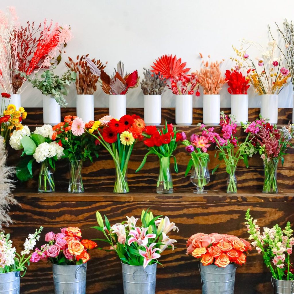 A display of flowers in vases on a wooden shelf.
