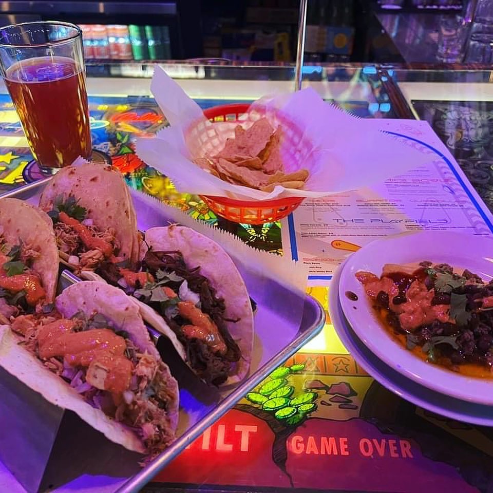 A tray of tacos and a beer on a bar.