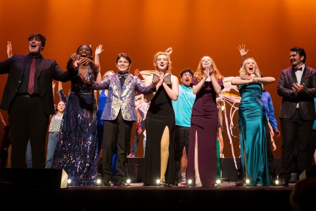 A group of Memphis students on stage with their hands up, taking on Broadway.