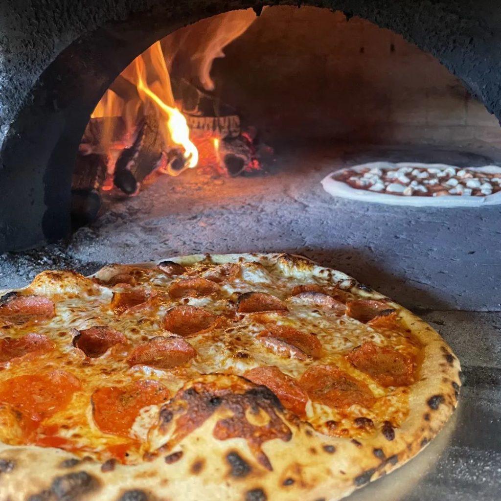A pizza sitting in a wood fired oven.