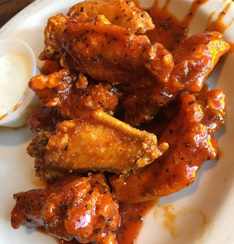 A plate of chicken wings with sauce and dipping sauce.