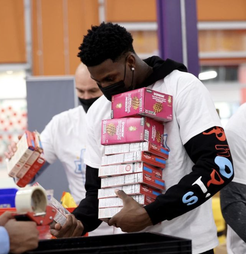 NBA star Dwyane Watson generously carries boxes of food to a food bank.