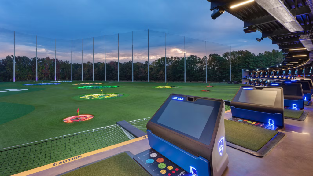 A modern driving range in Memphis equipped with targets, artificial turf, and individual player bays with digital screens at dusk. Perfect for those under 21 looking for things to do.