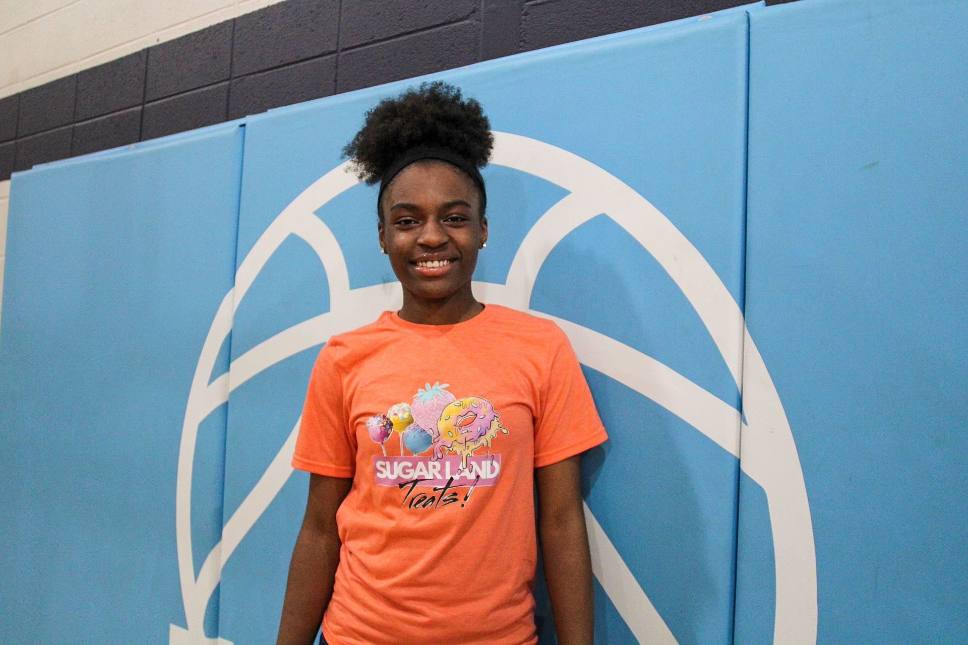 A young girl in an orange t-shirt standing in front of a basketball court at Memphis Athletic Ministries.