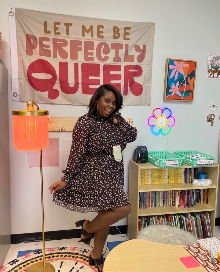 A woman posing in a classroom with a sign that says let me be perfectly queer during Teach901.