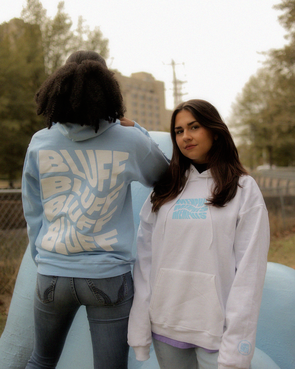 Two women posing in front of a blue hoodie.