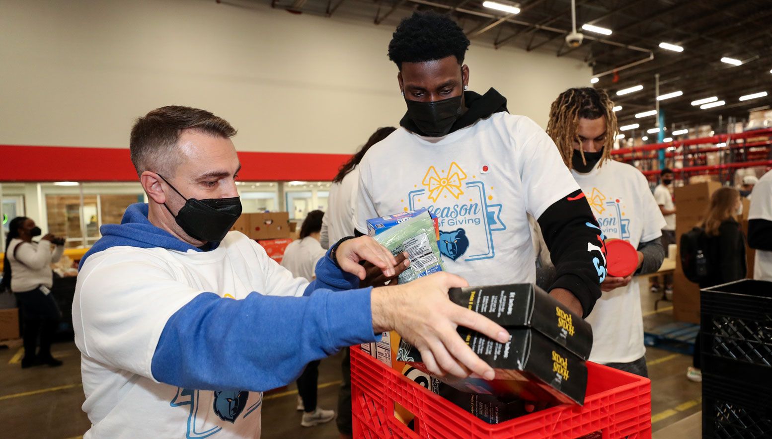 A group of men in masks are organizing boxes in a warehouse for Giving Tuesday.