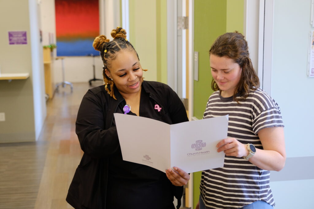 Two individuals reviewing a health document together in a corridor.