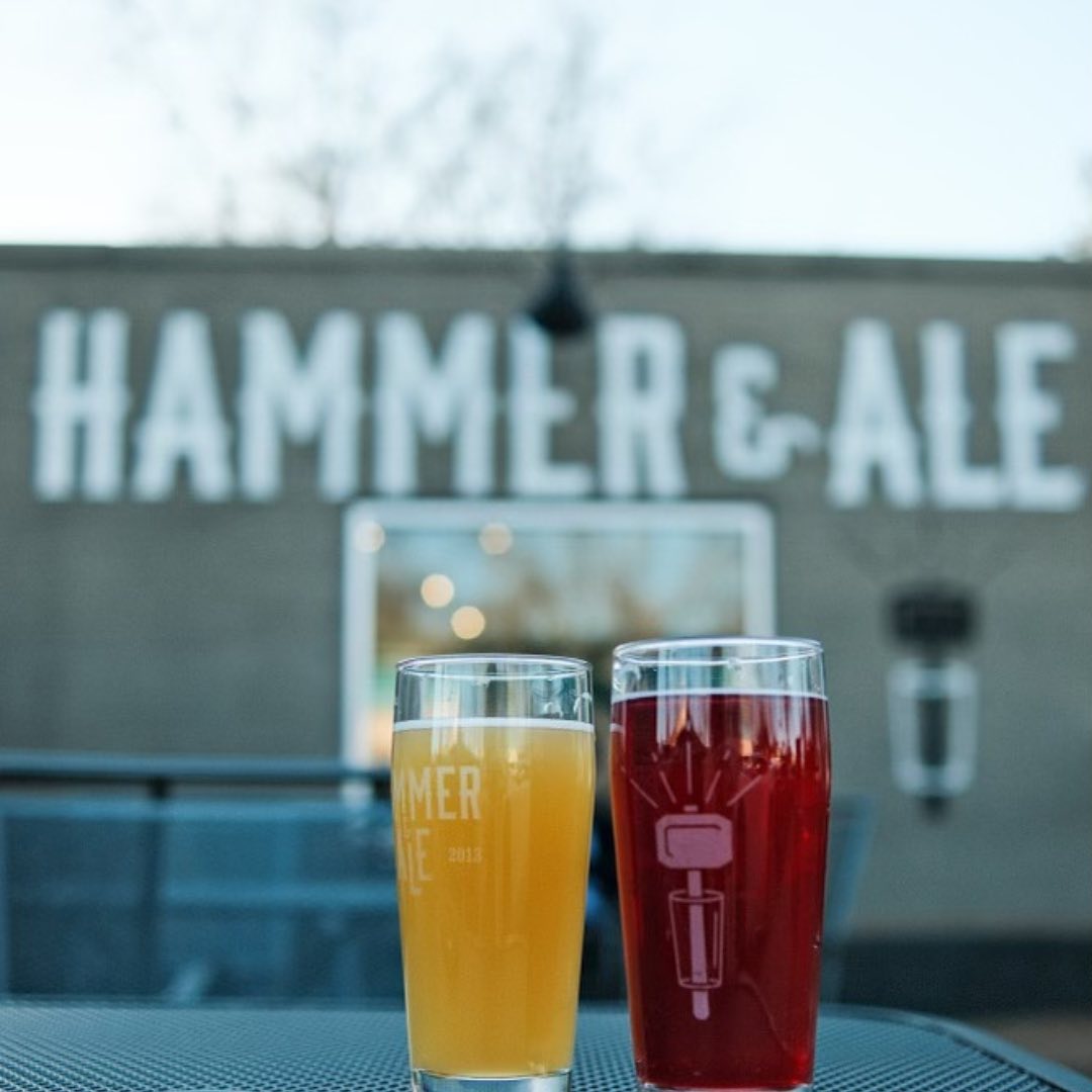 Two glasses of beer on a table, one amber and one red, at Memphis Breweries, with a "hammer & ale" sign blurred in the background.