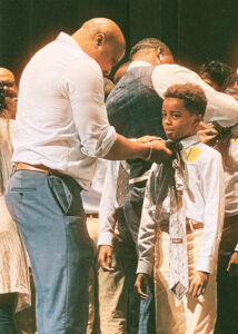 Celebrating Local Education: The 2nd Annual Tie Ceremony at Grizzlies Prep, where a man is tying a boy's tie.