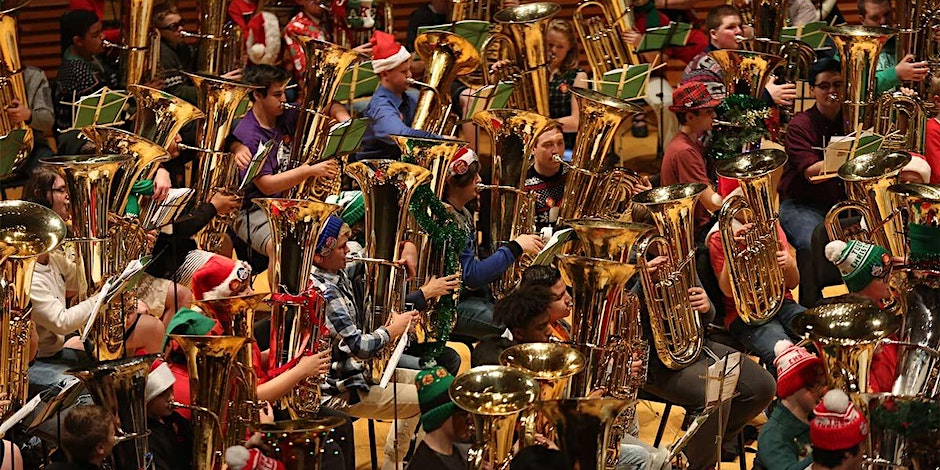 A large group of people playing tubas in a large auditorium.