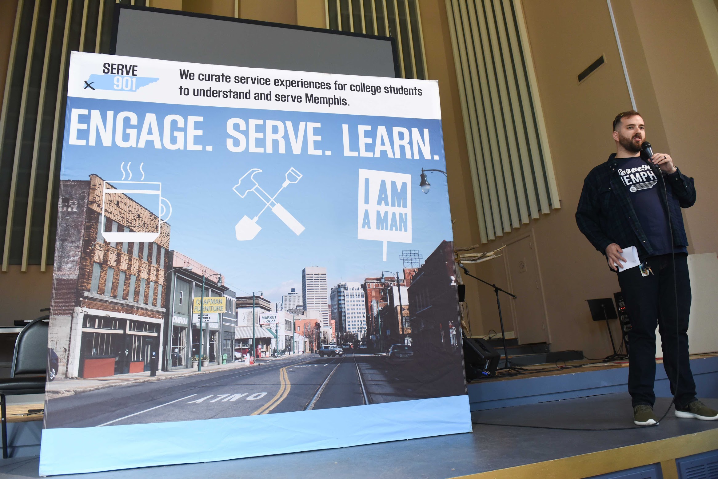 A man standing in front of a sign that says engage serve learn during spring break in Memphis.