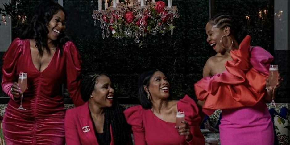 A group of women in pink dresses are smiling at each other at the Galentine's Soirée organized by Visions Event Studio.