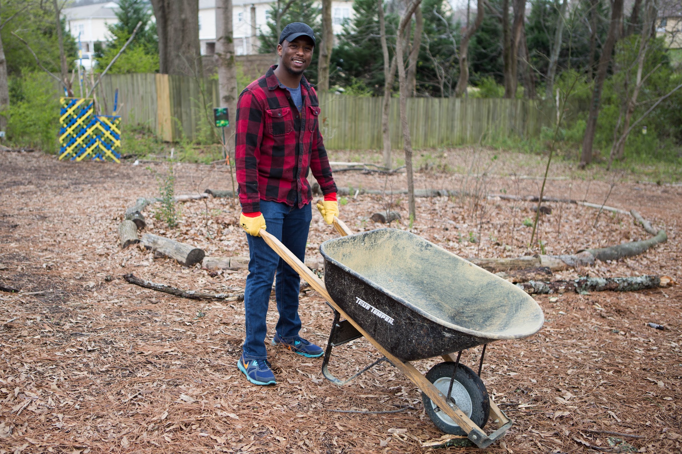 A man with a wheelbarrow in a wooded area during spring break.