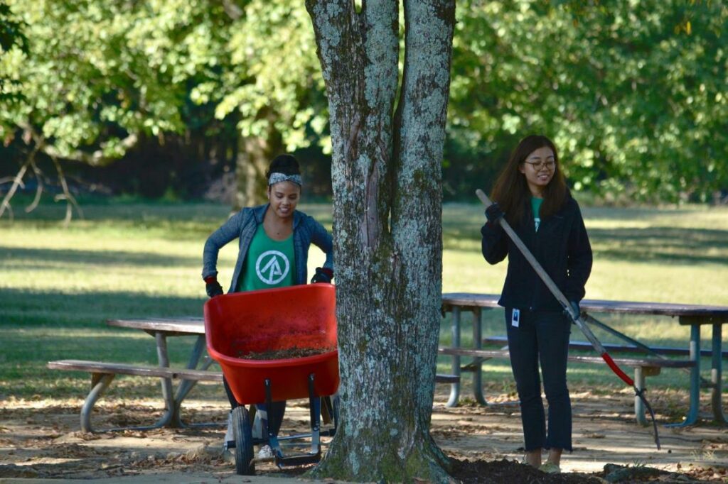 Two women volunteering with Volunteer Odyssey are pushing a wheelbarrow in a park.