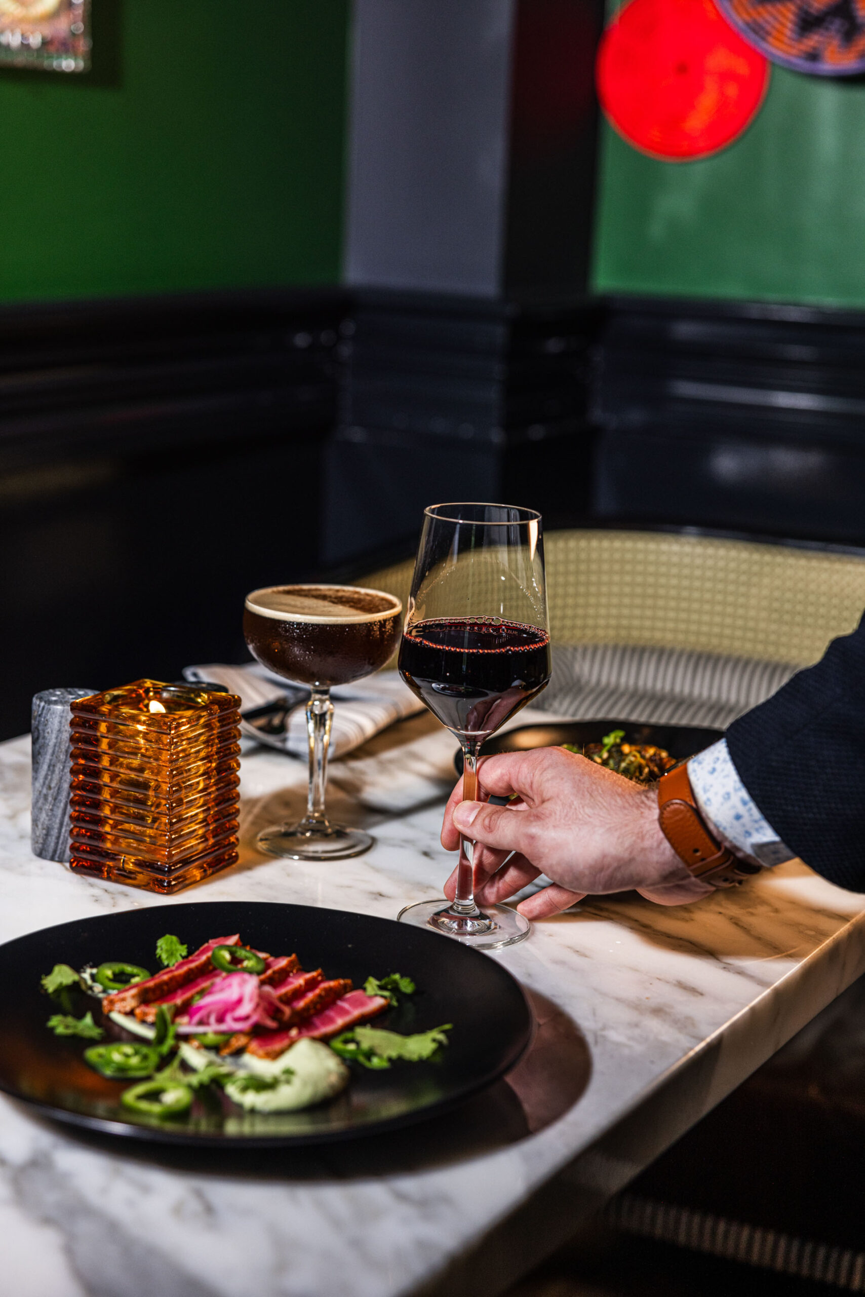 On Valentine's Day, a man elegantly holds a glass of wine and a plate of delectable food.