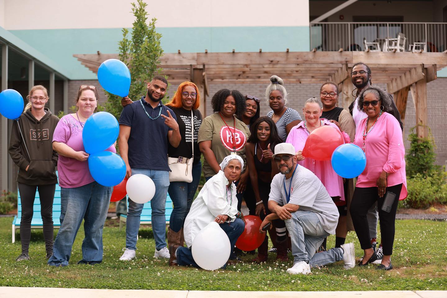 A diverse group of people from Memphis nonprofits posing with red, white, and blue balloons outside a building.