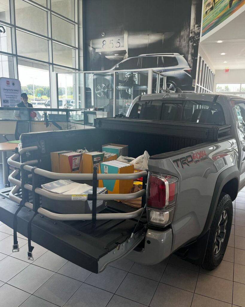 A pickup truck with an open tailgate is parked inside the Chuck Hutton Toyota dealership, with the bed containing several cardboard boxes and packages.