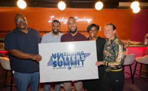 Group of five individuals holding a sign for the "Mentoring Matters Summit" in TN, posing together with smiles.