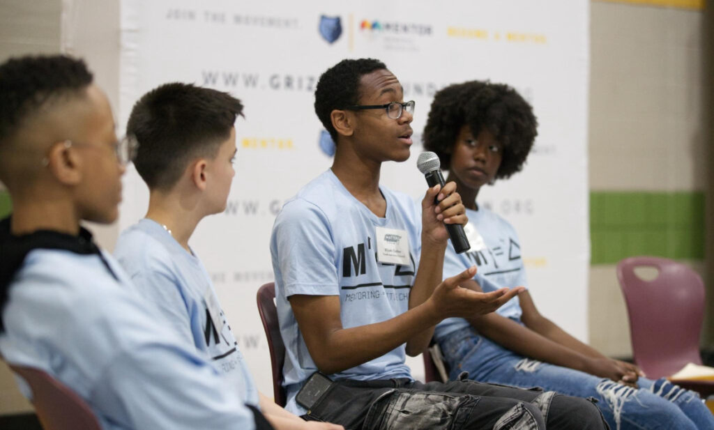 A young person speaks into a microphone during the Mentoring Matters Summit panel discussion while others listen.