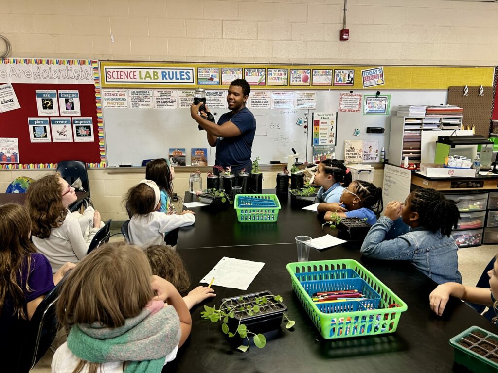 A science teacher demonstrating a sustainable experiment to an attentive classroom of elementary students.