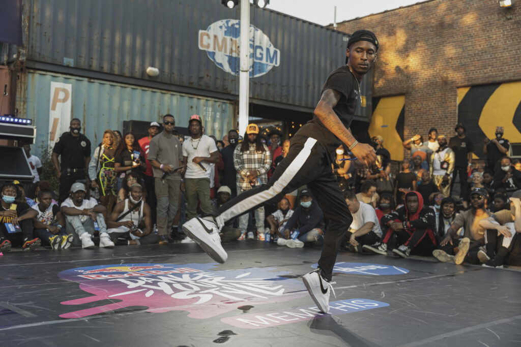 A person performing a dance move at the Red Bull Dance Your Style event with an audience watching in the background.